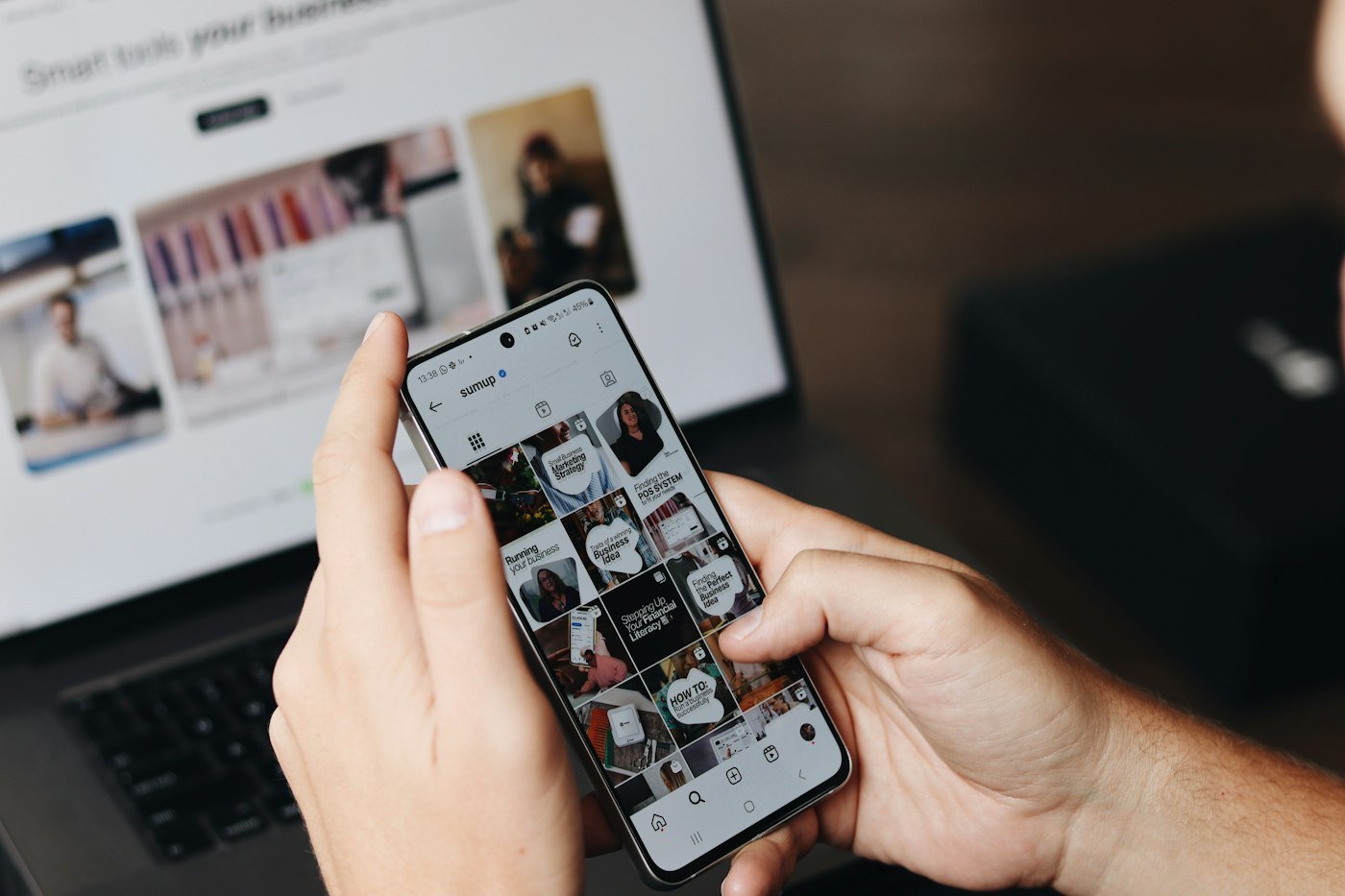 Person reviewing an ad on a phone in front of a laptop